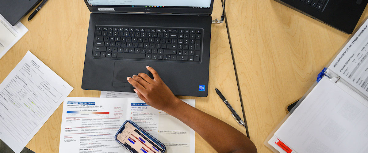A student at a computer with a phone in the foreground.