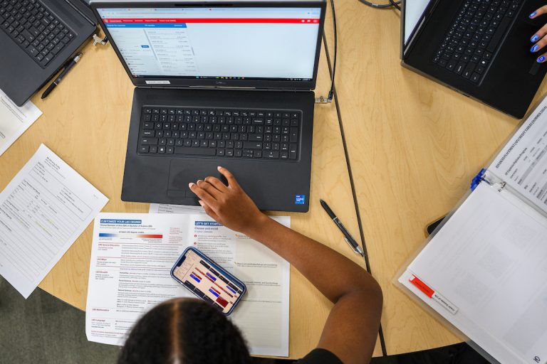 A student with a laptop and phone, registering for class.